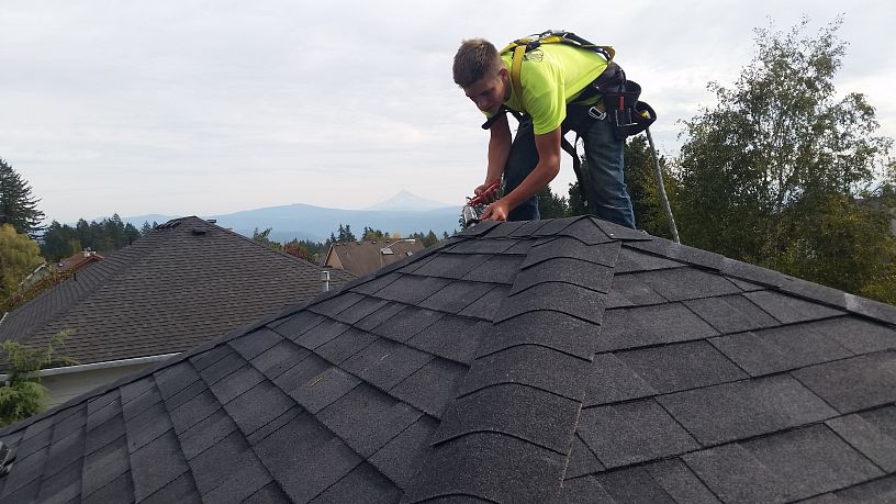 A close-up of an expert installing asphalt shingle on a residential roof replacement,